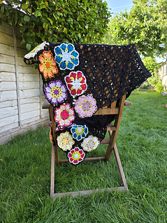 Black lace rectangular shawl with bright floral granny square border at short ends draped over chair