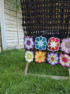 Black lace rectangular shawl with bright floral granny square border at short ends draped over chair
