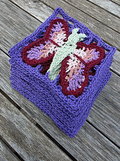crochet lace squares with colourful butterfly design  in blues purples, pinks and green stacked on a wooden slatted table