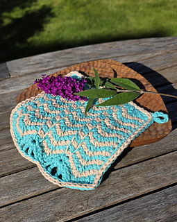 Turquoise and beige striped chevron stitch crocheted cloth on a wooden table, topped with purple flowers and green leaves in sunny outdoor setting