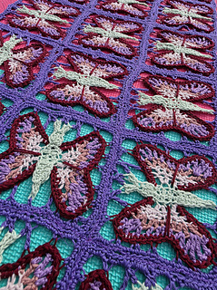crochet lace shawl with colourful butterfly design  in blues purples, pinks and green on a green foam mat (close)