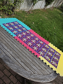 crochet lace shawl with colourful butterfly design  in blues purples, pinks and green on foam mats 