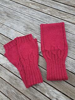 Pair of deep red cable knitted fingerless gloves shown with matching headband (not included in Mitts pattern) lying on a weathered grey wooden slatted table.