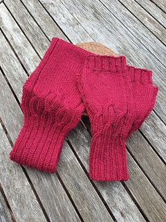 Deep red cable knitted headband and matching pair of fingerless gloves (not included in Headband pattern) lying on a weathered grey wooden slatted table.