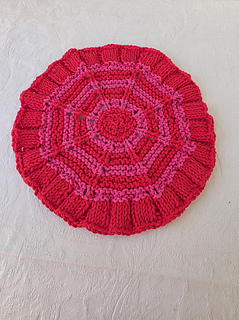 Red knitted circular washcloth with pink stripes on a white textured cloth.