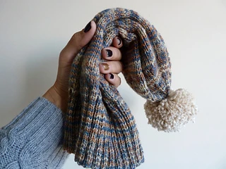 A hand holding a neutral coloured Sockhead hat with a beige pom pom.