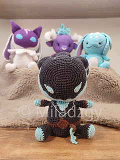 Thresh from League of Legends, crochet toy made by amigurumi technique. Used dark grey, turqoise and brown yarn. Front side, sitting at the table. There are Kindred, Alistar and Fizz sitting in the background.