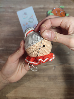 Crochet Mrs. Claus doll wearing a red collar with white details and gray hair in a bun. Sewing the eyes onto the face.