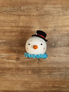 Crocheted snowman with white round head, carrot nose, collar, and small black hat. Put on the table.