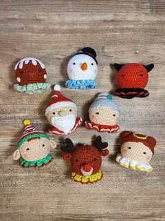 Collection of handmade crocheted Christmas dolls displayed together, including a devil, angel, Santa Claus, Mrs. Claus, gingerbread person, elf, snowman, and reindeer, arranged side by side on a neutral background.