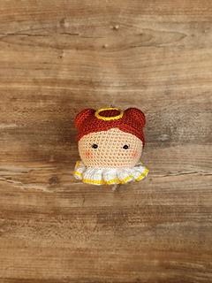 Crochet amigurumi style Christmas bauble. Brown hair with two buns, yellow halo at the top of the head and white-yellow collar. Lay on the table.