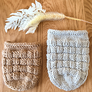 Two knitted  jar cozies, one beige and one gray, on a wooden surface with decorative floral elements.