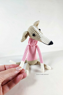 Elegant amigurumi Italian greyhound in a pink sweater holds out a slender paw to his crocheter.