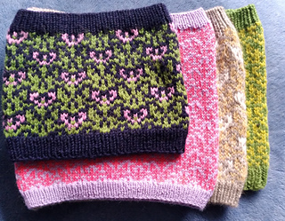 A stack of different versions of Hope Grows Roots Cowls. Three-Colour DK narrow (and off-gauge) and short, two-colour fingering narrow and tall, three-colour DK wide and tall, two-colour DK wide and tall.