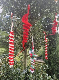 Red and white crocheted spiral Christmas ornaments hanging from a tree branch outdoors