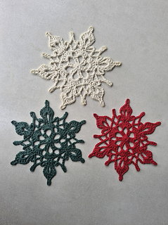 Three crocheted snowflake ornaments in cream, dark green and red lace on a light surface