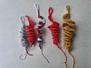 Crocheted spiral Christmas ornaments in mustard, red, white and gray lying on a light surface